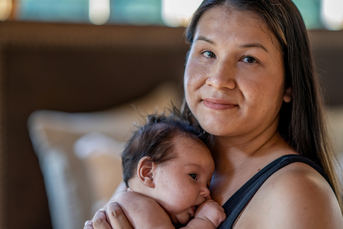 An Indigenous woman smiling while staring at the camera while holding a baby