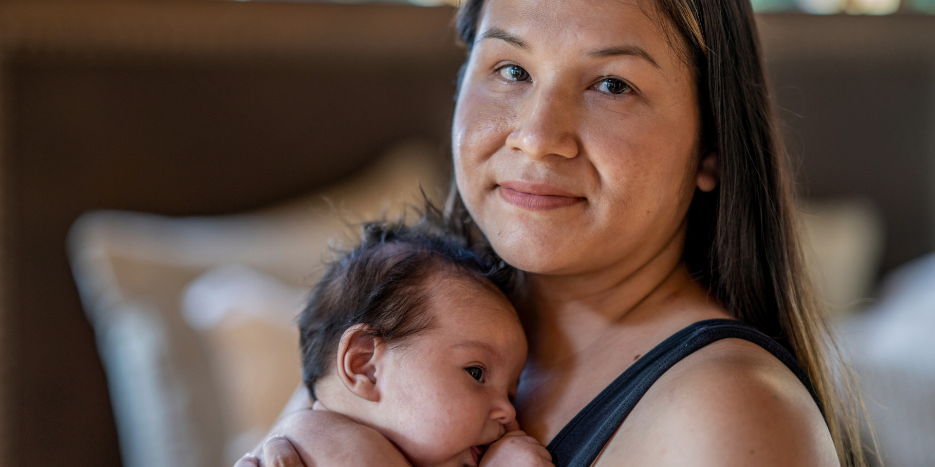 An Indigenous woman smiling while staring at the camera while holding a baby